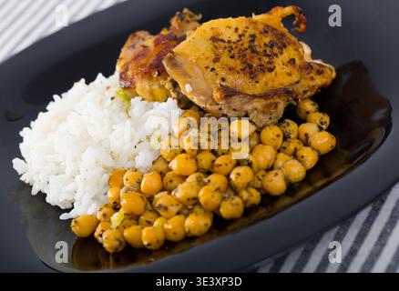 Cuisses de poulet cuites au four avec riz, garbanzos sur assiette noire Banque D'Images