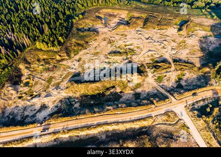 Vue aérienne d'une carrière de sable active avec plusieurs routes et pistes de véhicules traversant le terrain sablonneux. Une forêt luxuriante borde le site, highlig Banque D'Images