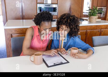 Diverses amies féminines se penchant sur le presse-papiers, pointant et examinant le papier avec des tasses au comptoir Banque D'Images
