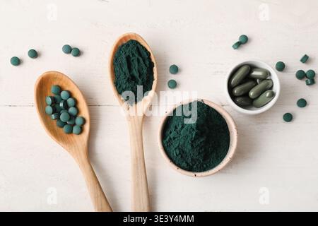 Bols de poudre de spiruline et capsules avec des comprimés sur fond de bois blanc Banque D'Images
