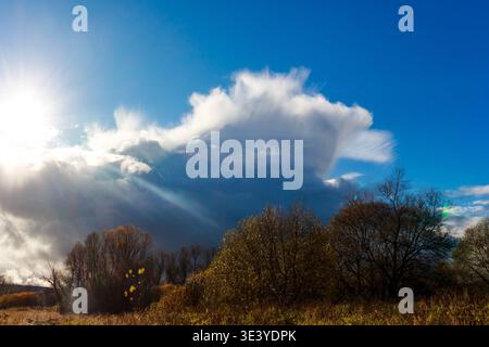 Un vaste nuage de cumulonimbus domine le ciel d'automne vibrant, des rayons de soleil spectaculaires traversent. La puissance brute de la nature se déploie sur un paysage d'automne serein Banque D'Images