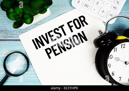 Message Invest for pension écrit sur papier placé sur une surface en bois bleu, à côté d'une loupe, d'une horloge, d'une calculatrice et d'une petite plante Banque D'Images
