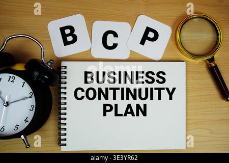 Texte du plan de continuité d'activité BCP écrit sur bloc-notes avec loupe et réveil sur fond de bois Banque D'Images