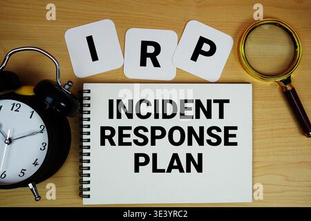 Texte du plan d'intervention en cas d'incident IRP écrit sur un bloc-notes avec loupe et réveil sur fond de bois Banque D'Images