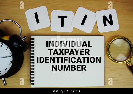 ITIN numéro d'identification de contribuable individuel texte écrit sur le bloc-notes avec loupe et réveil sur fond de bois Banque D'Images