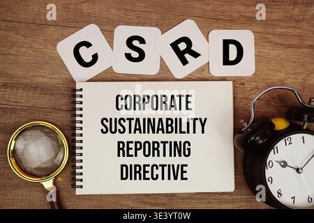 CSRD Corporate Sustainability Reporting directive texte écrit sur bloc-notes avec loupe et réveil sur fond en bois Banque D'Images