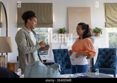 Homme tenant l'article de bébé et femme enceinte asiatique portant chemisier orange debout au pied du lit Banque D'Images