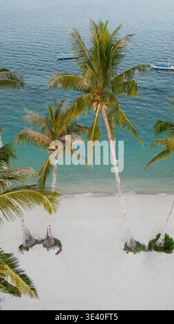Vue aérienne d'une plage tropicale avec de grands palmiers, du sable blanc et des bateaux traditionnels sur l'eau turquoise à Siargao, Philippines. Banque D'Images