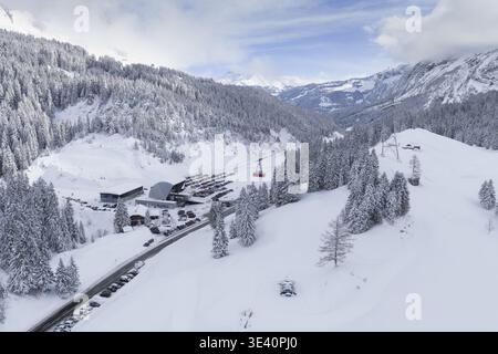 Vue aérienne d'une vallée enneigée berçant une station de remontées mécaniques et une route sinueuse, entourée d'arbres enneigés, Ormont-dessus, Vaud, Suisse. Banque D'Images