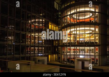 Une vue nocturne époustouflante de l'architecture moderne à Berlin, en Allemagne. L'image montre un complexe de bâtiments avec de grandes façades en verre incurvées illum Banque D'Images