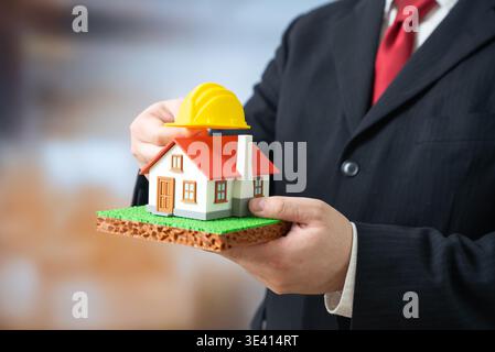 Un homme d'affaires pose un casque de construction jaune sur sa maison. Rénovation et reconstruction de logements. Logements et infrastructures abordables. Urbain Banque D'Images