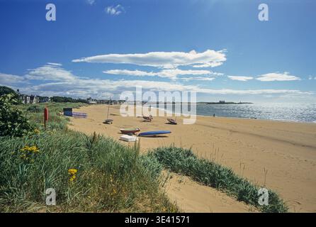 Journée d'été ensoleillée à la plage d'Elie avec des voiliers sur du sable doré, des dunes herbeuses, des maisons côtières et une mer étincelante sous un ciel bleu. Pays balnéaires sereins c Banque D'Images