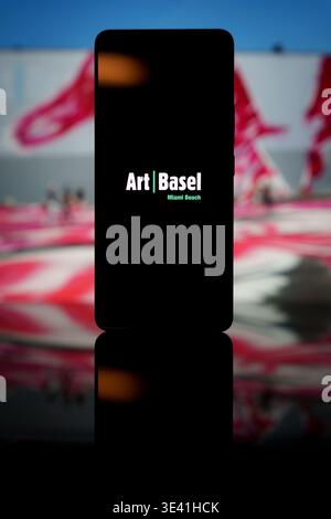 Logo Art Basel Miami Beach affiché sur un écran de smartphone avec un fond mural artistique flou, représentant une foire internationale d'art contemporain Banque D'Images
