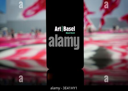 Logo Art Basel Miami Beach affiché sur un écran de smartphone avec un fond mural artistique flou, représentant une foire internationale d'art contemporain Banque D'Images