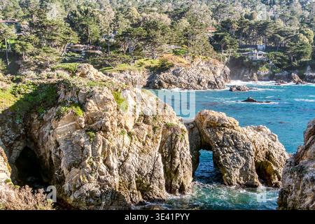 Les falaises ensoleillées encadrent les vagues turquoises de l'océan. Des roches accidentées jaillissent de l'eau, altérées par le temps. Des arbres verdoyants couronnent des rivages lointains. ECLAIRAGE lumineux Banque D'Images