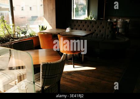 Intérieur de café moderne avec tables en bois, chaises moelleuses et lumière chaude du soleil à travers la fenêtre. Concept de confort, d'hospitalité et d'espace salle à manger élégant. Banque D'Images
