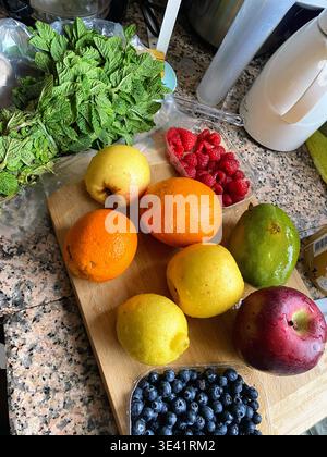 Fruits frais et feuilles de menthe vibrantes disposés sur un comptoir de cuisine, créant une scène de préparation des aliments propre, naturelle et accueillante. Banque D'Images