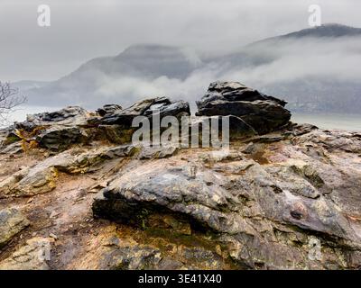 Affleurement rocheux humide au-dessus de la rivière Hudson dans les Hudson Highlands, avec du brouillard et des nuages bas à travers les montagnes de l'État de New York. Banque D'Images