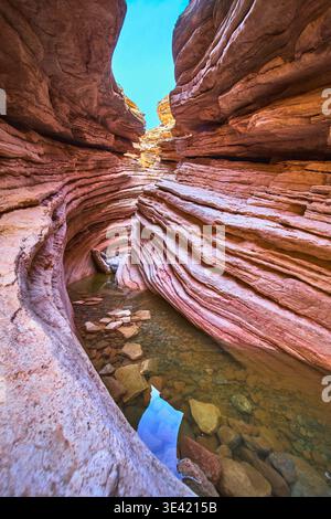 Couches de roche colorées de Slot Canyon avec piscine tranquille et ciel ensoleillé Banque D'Images