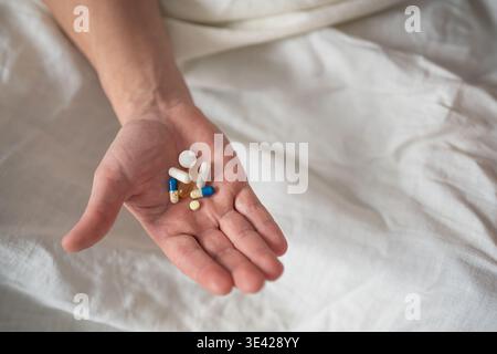 Tas de diverses pilules colorées et capsules dans la main sur fond de feuille blanche, vue de dessus. Homme senior prenant des médicaments, tenant de nombreuses pilules en main. Tous les jours Banque D'Images