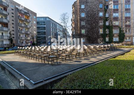 Mémorial de synagogue composé de rangées de chaises disposées en plein air sur une place entre des blocs d'appartements préfabriqués et un immeuble de bureaux moderne : chaises en bois vides disposées en rangées, prêtes pour un service commémoratif. Leipzig, Saxe, Allemagne Banque D'Images