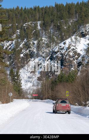 Russie, République de Bachkortostan, village d'Irgizly - 15 mars 2026 : Land Rover Freelander 2 rouge sur une route enneigée à travers des falaises rocheuses et des forêts de pins Banque D'Images