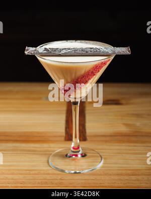 Cocktail crémeux dans un élégant verre à martini. La garniture de sucre rouge ajoute une touche audacieuse. Ruban argenté drape le bord gracieusement. La surface en bois améliore rustique Banque D'Images