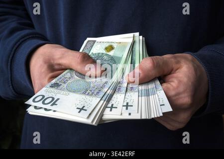 Acheter avec des économies. Un homme tient des billets de banque polonais de cent zloty dans ses mains. Banque D'Images