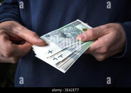 Acheter avec des économies. Un homme tient des billets de banque polonais de cent zloty dans ses mains. Banque D'Images