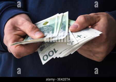 Acheter avec des économies. Un homme tient des billets de banque polonais de cent zloty dans ses mains. Banque D'Images