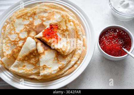Crêpes fines faites maison avec caviar rouge et crème gros plan. Crêpes salées avec caviar de poisson de saumon. Semaine des crêpes Maslenitsa petit déjeuner traditionnel. Banque D'Images