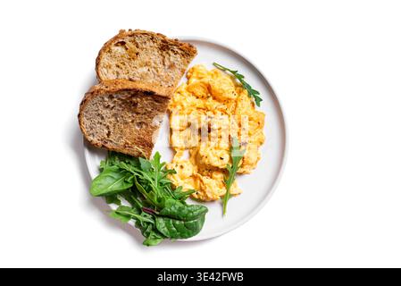 Œufs brouillés avec des légumes verts pour un petit déjeuner céto sain. Assiette d'œufs brouillés avec mélange de salade roquette isolé sur fond blanc, vue de dessus. Banque D'Images