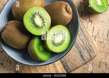 Kiwi fruits dans un bol en bois. Gros fruits entiers et demi-morceaux de kiwi vert. Kiwi mûr frais. Modèle d'alimentation saine biologique. Banque D'Images