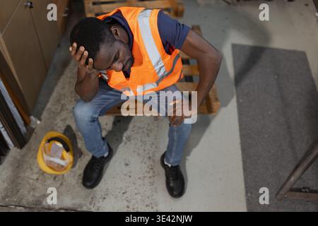 Travailleur afro-américain se sentant submergé et fatigué, prenant une pause dans le stress extrême du travail et l'épuisement professionnel dans un entrepôt de stockage industriel. Banque D'Images