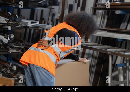 Femme logistique et ouvrier d'entrepôt souffrant de maux de dos après manipulation manuelle, levage et transport de boîte en carton lourde. Banque D'Images