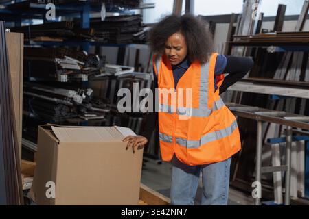 Femme logistique et ouvrier d'entrepôt souffrant de maux de dos après manipulation manuelle, levage et transport de boîte en carton lourde. Banque D'Images