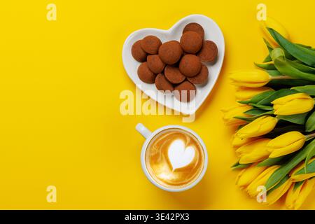 Café avec mousse de lait en forme de coeur sur fond jaune avec des tulipes jaunes, concept de printemps lumineux Banque D'Images