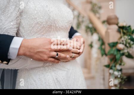 Fermer les mains attachées sur la taille des brides montrant les anneaux de mariage et le poignet de costume, texture de tissu doux, . Banque D'Images
