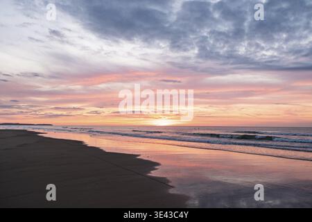 Beau lever de soleil sur une scène de plage sereine avec le ciel coloré et les vagues calmes de l'océan reflétant la lumière du soleil Banque D'Images