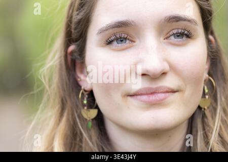 Portrait serein d'une jeune femme avec des boucles d'oreilles, dans la lumière extérieure naturelle, mettant en valeur sa beauté et son élégance Banque D'Images