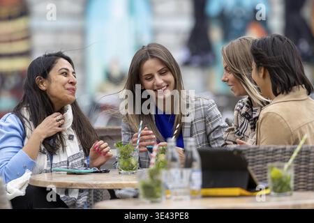 Quatre amis passent un bon moment, rient et prennent un verre dans un café en plein air tout en discutant Banque D'Images