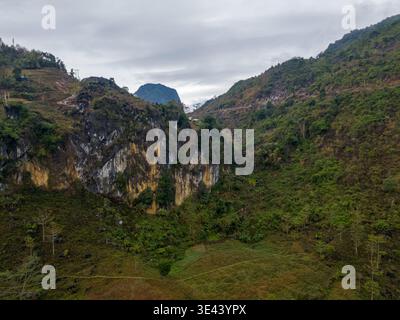 Près de me Pja Pass, Vietnam – 13 janvier 2024 : falaises rocheuses et collines verdoyantes s’élèvent au-dessus d’une vallée rurale sous un ciel couvert dans le nord du Vietnam. Banque D'Images