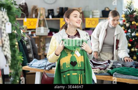 Positive jeune femme choisissant un pull dans le magasin de vêtements Banque D'Images