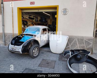 Une Volkswagen Beetle vintage subit une restauration de carrosserie et de peinture dans un garage d'angle de rue à Barcelone, avec son capot et ses ailes enlevés pour Banque D'Images