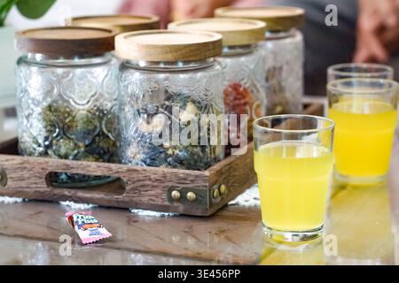 Pots décoratifs avec couvercles en bois et un verre de jus jaune disposés sur un plateau à côté d'une plante en pot. Banque D'Images