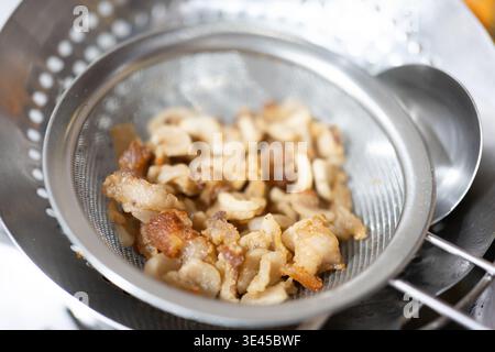 Bits de ventre de porc croustillant égouttant dans la passoire en métal, préparation de la cuisine chinoise, scène de cuisine Banque D'Images
