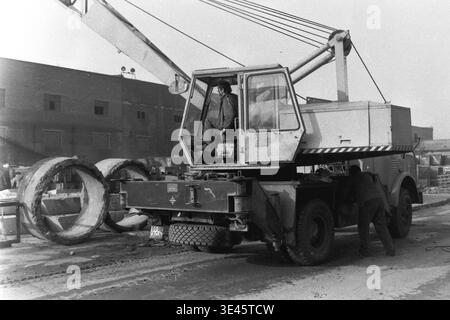 Sloviansk, avril 1989, cour d'usine AIZ. La direction de l'usine et les travailleurs participent à une journée traditionnelle de nettoyage de bénévoles de subbotnik au printemps. Un homme est vu en train de conduire une grue de camion mobile lourd tandis qu'un autre assiste à l'extérieur près de grands anneaux industriels en béton. Ils travaillent ensemble pour nettoyer le territoire de l'usine des débris de construction et organiser l'espace extérieur. Cette scène souligne le fort esprit collectif et la responsabilité partagée des travailleurs dans le Donbass pacifique. Banque D'Images
