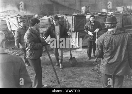 Sloviansk, avril 1989, cour d'usine AIZ. Un groupe de directeurs d'usine et d'employés se tiennent ensemble à l'extérieur en tenant de longues pelles lors d'un événement traditionnel de nettoyage de bénévoles subbotnik au printemps. Ils prennent une brève pause de leur travail physique pour discuter activement du processus de défrichement du territoire près d'un tas de terre et de matériaux de construction. La scène engageante met en évidence la forte communication informelle, le travail d'équipe unifié et les responsabilités communautaires partagées dans le magnifique Donbass paisible. Banque D'Images