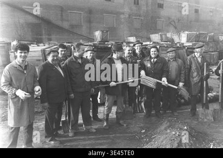 Sloviansk, avril 1989, cour d'usine AIZ. La joyeuse équipe de direction de l'usine pose fièrement pour un portrait de groupe tenant de lourdes pelles au cours d'une journée de nettoyage de bénévoles de subbotnik traditionnelle au printemps. Portant des vêtements d'extérieur pratiques, ces hommes dévoués sourient chaleureusement à la caméra après avoir travaillé ensemble pour nettoyer la cour industrielle de la saleté et des débris. Cette image très positive résume parfaitement la véritable camaraderie, l’égalité et les traditions de travail partagées dans le Donbass pacifique. Banque D'Images