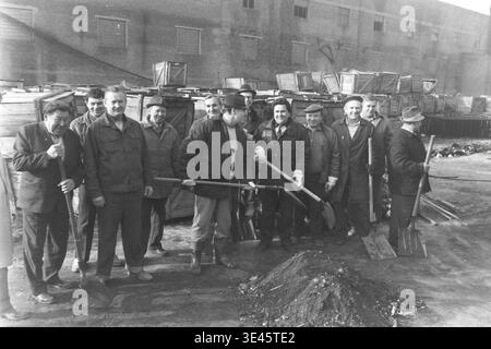 Sloviansk, avril 1989, cour d'usine AIZ. La joyeuse équipe de direction de l'usine pose fièrement pour un portrait de groupe tenant de lourdes pelles au cours d'une journée de nettoyage de bénévoles de subbotnik traditionnelle au printemps. Portant des vêtements d'extérieur pratiques, ces hommes dévoués sourient chaleureusement à la caméra après avoir travaillé ensemble pour nettoyer la cour industrielle de la saleté et des débris. Cette image très positive résume parfaitement la véritable camaraderie, l’égalité et les traditions de travail partagées dans le Donbass pacifique. Banque D'Images